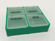This photograph shows a green pill box with four compartments. The compartments are labeled MORNING, NOON, EVENING, AND BEDTIME 