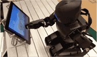 : Picture of our robot, Darwin, interacting with the tablet. The robot is kneeling in front of the Android tablet, extending its right arm forward to reach out to the screen. The robot is moving the object on the screen while its eyes are following the movement of the manipulated object