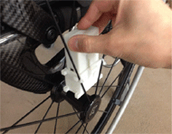 Figure 2: The picture displays the GWRM attached to its holder, zip-tied to the spokes of the wheelchair. The GWRM holder is white in color and has a single buckle design. Users are instructed to zip-tie the holder to the spokes prior to inserting the GWRM. The buckle provides a clicking sound when the GWRM has been properly locked into the holder. 