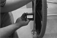 A man is holding an inclinometer against an aluminum bar. The bar has bolts threaded into its ends, and the bolt tips have plastic endcaps that are touching the wheel at the top and the bottom of the rim. The inclinometer is reading a value of 00.50 degrees. 