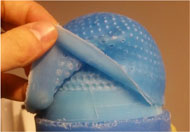 The two layers of the distal end of the perforated prosthetic limb liner can be seen here prior to bonding them permanently together. This figure shows a mans hand peeling back an outer layer of a double layer perforated silicone prosthetic limb liner. 