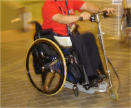 Picture of manual wheelchair user demonstrating driving of manual wheelchair with scooter power add on option. 