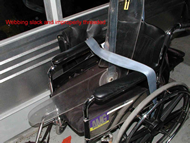 Photo showing improper routing of the vehicle-anchored lap belt over both armrests of the wheelchair in case WC-006.