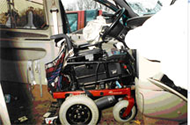 Side view of the driver’s wheelchair in case WC-014 secured in the docking tiedown device, with the deployed steering-wheel airbag draped into the wheelchair seat.