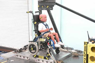 Figure 2. Pre-test photo of the second prototype. The figure shown a front oblique view of a three-year-old sized ATD secured by a five-point harness to a pediatric wheelchair.  This prototype has new aluminum brackets that strengthen the seat-to-seatback junction and anchor the lap belt portion of the harness.