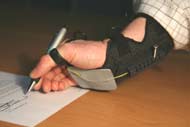 This figure shows the key grip orthosis being used to assist the holding of a pen.  The participant is signing their name with the pen.