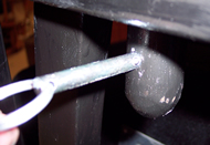 Image shows a side view of the desk attachment that fits into the constructed armrests of the chair.  A safety pin is shown being inserted into the desk dowel to lock the desk in place.