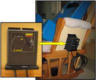 Image of the speed control. The speed control is a black box with dimensions 5.5” x 3.5” x 3.8”. On its front side is an on/off switch and a dial ranging from 0 to 10. The speed control is mounted on a vertical panel of wood underneath the arm of the chair.   