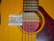 Image shows the overhead view of the mounting track attached to the guitar. The mount attaches like a clamp to the side of the guitar soundhole. The track is positioned perpendicularly and in close proximity to the guitar strings. Two ball protrusions stick out from the track and are used to guide the strumming component into place. 