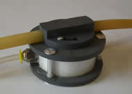 Figure 6 shows the “Sandwich Style” body design of the valve, which uses a piece of stock tube (white), two plastic discs on both ends, and screw posts for assembly.  This body style is designed for the “do-it-yourself” customer wanting to build their own valve using stock materials.  The top of the valve is sealed by the diaphragm while the bottom is sealed with an adhesive.  The sipping tube can be removed by pushing on the yellow release of the quick connect.  The valve shown is a prototype and is opaque as opposed to the clear plastic which would normally be used during building. 