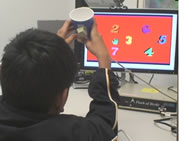 Image shows a boy holding a blue paper cup with both hands, in front of a computer monitor that has the numbers 2-7 randomly arranged on the screen. 