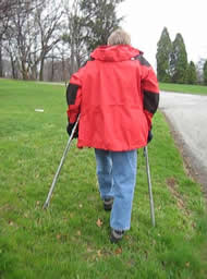 This photo shows the prototype crutches being used on a cross slope, a grassy hillside. The left crutch is shorter than the right because the ground slopes down to the right. 