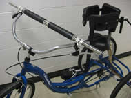 Photo 1 shows a nearly complete view of the client’s tricycle with the modifications for the custom tricycle brake system, including both the custom handlebar and the adapted brakes. Other features seen are the torso brace and one of the two-foot sandals that the client’s family installed themselves.  