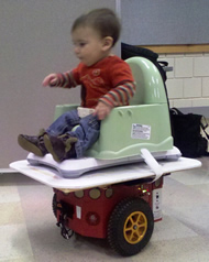 Image shows the set up for our balance board control method.  The infant sits in the commercial seat on top of the balance board, supported by the custom platform.   