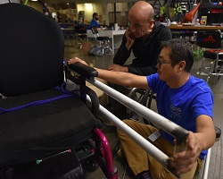 Two teammates measure the device prototype with the power wheelchair