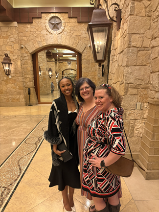 Three women in dressy clothes standing in a medieval looking hallway