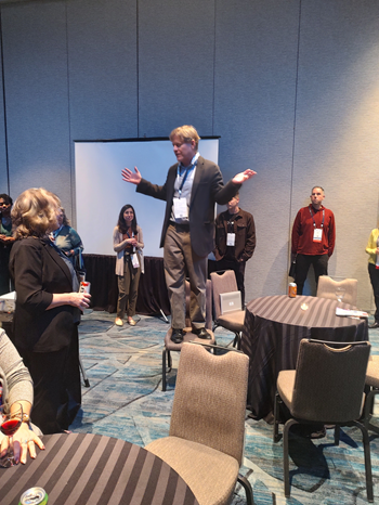 Man standing on top of a chair welcoming people at a reception 
