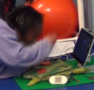 Picture of children with disabilities using the plush switch. There are two images. The top image shows a young girl interacting with the tablet using the plush switch. The bottom image shows a young boy interacting with the tablet using the plush switch.  