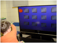 Picture of the subject wearing the motion tracker on his right hand while playing the memory game by reaching to move the representation of his hand on the game screen to turn the upper-left block. 
