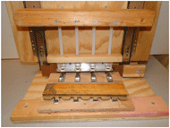 Figure 5 is a photo of a press that can produce 4 completed assemblies at once. The washers are positioned in holders above the ridged posts.  Pressing downward on a bar pushes the washers onto the posts. 