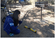 Photo of a woman at a campsite squatting down to measure the grade of the clear ground space in front of a cooking grill with a SmartToolTM