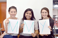 From left to right, holding up white signs with letters on them: Nina Ligon, holding a green M; Devika Patel, holding another green M; and Claire Jacobson, holding a blue Y.