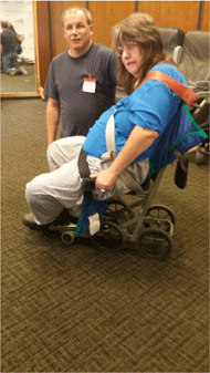 Figure 3 Left is a side view of a non-ambulatory large female  seated in an Columbia Aislemaster boarding chair. The person is not able to be secured  in the boarding chair. The person is hanging over the seat. The straps are not able to be positioned properly. The foldable arm supports cannot be moved down into the usable position because they will not fit this person’s girth.
