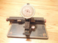 The Dial Typeriter requires the user to turn a large dial to select the letter to be typed, then press a bar to impress that letter on the paper.  There is also a lever to produce a space.