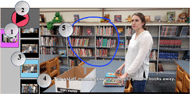 This image displays a screenshot view of the EasyVSD app from the view of the participant. The majority of the image shows the still frame of a videoVSD for the task of putting books away. Aside from navigation icons and a play/pause button positioned vertically on the left-hand side of the screen, the videos filled the majority of the screen of the tablet. The image is of an individual standing at a table in a library. There are several books in two organized piles in front of the individual as well as the empty box that was used to transport the books to the table. At the bottle of the image, a text label reads the steps for the task, “Tell a staff member you are going to put the books away.” This text is accompanied by a circle with the number 4 inside. Additionally, a dark blue outline of a circle accompanied by a circle with the number 5 inside represents the hot spot for the communicative turn within the skill. Aside from navigation icons and a play/pause button positioned vertically on the left-hand side of the screen, the videos filled the majority of the screen of the tablet. To the left of the image, there are navigating tools for the participant to use the app. In the top left corner is a play/pause button, labeled by a circle with a number 2 in it. When a video is playing, the play button becomes a pause button. Below the play/pause button, the app contains two menu bars positioned vertically. The menu bar on the left contained a single still VSD (i.e., thumbnail representations) displaying the current task the participant was completing. This single VSD is labeled by a circle with the number 1 inside and is an image in a square shape outlined in purple. The thumbnails on the right side, labeled by a circle with a number 3 inside, displayed each of the still VSDs within the task and depicted the start of each step or video. These thumbnails were used to navigate between video segments and were highlighted with a blue border to indicate the video currently playing. At the bottom of this image, is a text box that relates each labeled part of the image to the corresponding number in each circle. The text reads, “Note: (1) topics for selection, (2) play button, which becomes a pause button when the video plays, (3) specific steps within each task, (4) text on screen that describes the current step of the task analysis, (5) hot spot for communicative turn”.  