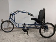 . The Freedom Concepts tricycle that was adapted This figure shows a picture of the Freedom Concepts tricycle that was required to be adapted. This tricycle resembles a typical recumbent tricycle, but features pedals with straps to help the user’s feet stay in place, handlebars that are used by pushing or pulling with hands designated for left or right steering, and a seat that provides a wide support for the buttocks, lower and upper back. This tricycle is recumbent, allowing the user to sit leaned back slightly with their legs in front of them.  