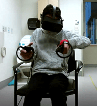 A front-facing photo is shown of Participant 1 with personal identifiers removed. The participant is seated, wearing the VR headset, and holding a left and right controller in each respective hand. A splint around the participants wrist and thumb can be seen on their left hand and their left elbow is raised. 