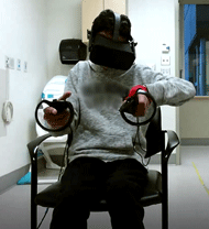 A front-facing photo is shown of Participant 1 with personal identifiers removed. The participant is seated, wearing the VR headset, and holding a left and right controller in each respective hand. A splint around the participants wrist and thumb can be seen on their left hand and their left elbow is raised.