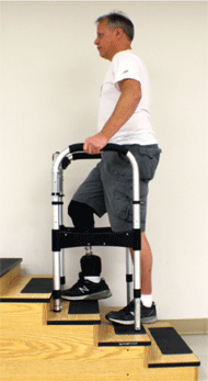Image of the Self-Leveling Walker in use during stair negotiation training.  The user is ascending the stairs with the walker in an ascending configuration; that is, the front legs are retracted and the rear legs are extended by the same amount so that there are four points of contact with the arm rails parallel to the ground. 