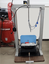 Figure 1. The impact damping test fixture uses a rigid hollow mold dimensioned according to the anatomy of a human buttock. It is filled with magnum lead shots held together with smooth cast to evenly distribute a weight totaling to 500N +/- 10N. A rigid plate is hinged at one edge and is used to support the cushion and indenter. The plate is propped up using a wooden block to an angle of 10 +/- 1 degrees. An alignment slab maintains the position in the antero-posterior direction and a laser pointer ensures consistent placement in the medio-lateral direction. The fixture uses a pneumatic system to raise and lower the indenter. 