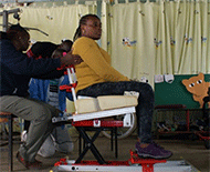 Figure 3 is a picture of three clinicians positioning a wheelchair user in the wheelchair simulator to position and take accurate measurements of the user. 