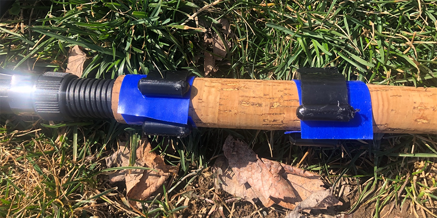 Brown fishing rod handle with blue dycem wrapped around in two sections held together with a black fishing rod clip.