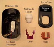 All of the parts of the Toothbrush Buddy are disassembled on a yellow background. From left to right: the black dispenser box is shown with the sliver piece of metal mounted on the back as the feedback mechanism. Next, is the white toothpaste suction shaped like a cylinder with a nozzle coming out of it. A grey skinny lever with a square opening and cylinders to mount. A black rectangular front cover with the toothbrush buddy logo on it. A red box shaped track with 3 hooks shown.