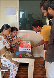 A eight year autistic child inserting the shapes on to the device to learn the basic shapes with the help of device, which is placed on a table along with the trainer
