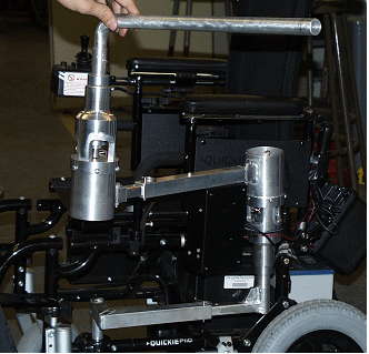 Picture of prototype:  This picture was taken of the prototype near its completion.  The picture shows the prototype attached to a wheelchair.  The picture focuses on the upper rotating joint, but also shows the telescoping arms and the location of the control unit.