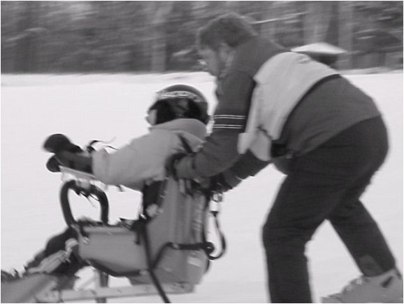 Figure 2. Bi-ski user on the slopes with dynamic armrest. The skier is shown in the sit-ski with his arms strapped into the dynamic armrests, followed by a companion skier.
