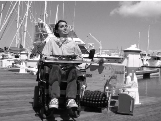 Figure 1: Todd in his power wheelchair, sitting on the dock with the seating support system and his ventilator propped next to him.