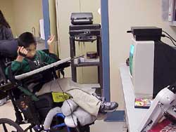 This photograph is the same student continuing to play PlayStation 2 using his DynaVox 3100. He accesses the spec switch with finger flexion. 
