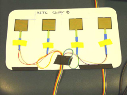 Photo. 1 depicts the MAM sensor array mounted on it rigid plastic backing but without the protective rubber envelope. Each square sensor is attached to a wire and all four are mounted in a row on a rigid pad. 