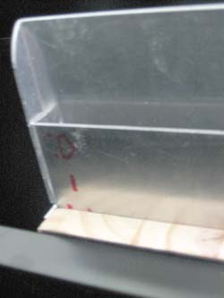 Image shows the bottom view of the envelope inserting aid channel. The top ledge of the channel is longer than its base. The gap between the ledge and the tray forms a channel for documents into the envelope.