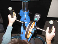 The first photo shows a subject turning the ergometer to the right.  The ergometer rests on a metal bar that pivots above the main arm of the GameCycle.  The two pieces are interfaced at the end of the arm closest to the subject.  