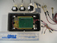 Photo shows the components of the datalogger. In the center of the photo is the open datalogger case, with datalogger circuit board inside.  In a row above the open case are the three tilt sensors and the three pressure sensors. A ruler is included in the image, showing that the case is approximately 8 inches long and 4 inches wide, and the tilt sensors are approximately 1 inch by 1 inch by 1 inch.