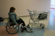 This photograph shows a client driving her manual wheelchair and pushing a shopping cart that is attached to the wheelchair using the unit that was developed.