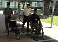 This photograph shows the mobile data collection system used on the test course to collect data. The operator is following the instrumented chair, while the subject is propelling through the test course in the instrumented chair. 