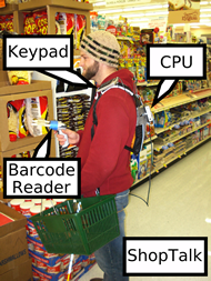 This image the ShopTalk system being worn by a user in the supermarket.  The computation device, a 1x3.75x5 OQO computer,  is mounted on a backpack.  The backpack also holds the base station for the wireless barcode reader.