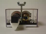 Image shows the front view of the strumming component. A mounting plate and a base plate are screwed together. The push and pull solenoids are enclosed in circular clamps and attached onto the base plates. The pick rod connected to the push solenoid plunger is connected to the pull solenoid plunger through a screw connection extending between both solenoids parallel to the base plates. 